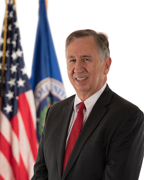 Portrait of Guy Cavallo standing in front of the American and OPM flags.